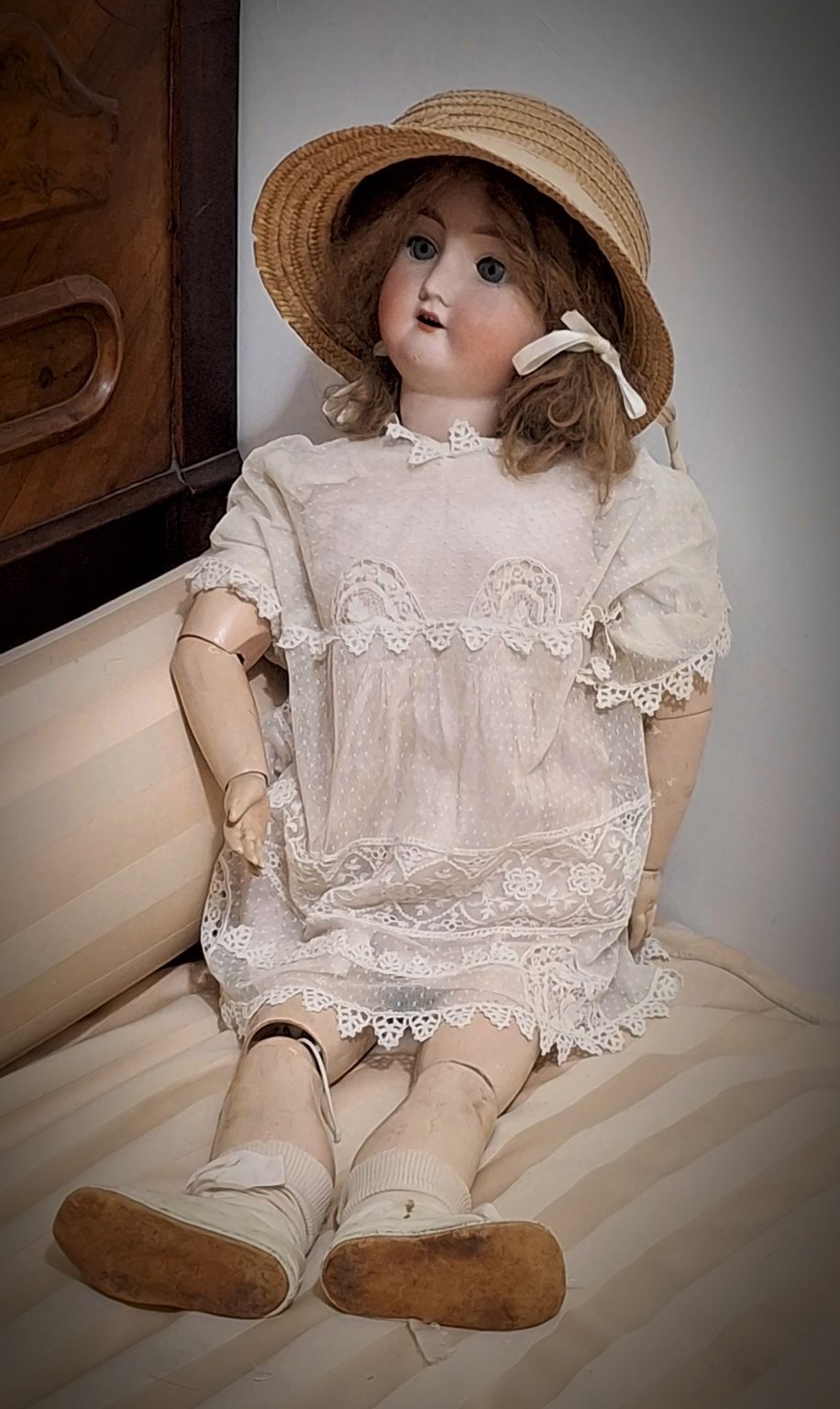 La bambola seduta sul divano letto, con il cappello di paglia, l’abito di pizzo bianco e le scarpe dalla suola consumata