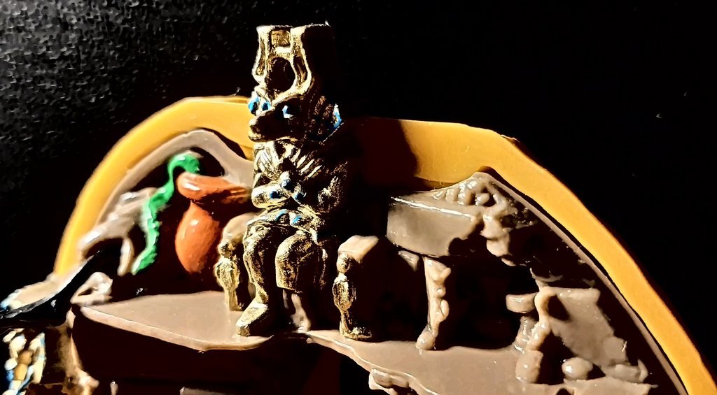 In cima alla parete, la statua d'oro seduta accanto a un vaso arancione con un serpentello verde